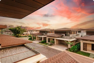 Row of modern, single-story homes with tiled roofs along a quiet street at sunset, pink and orange sky above.